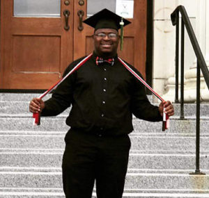 Alumni Isaiah smiling on steps with graduation cap
